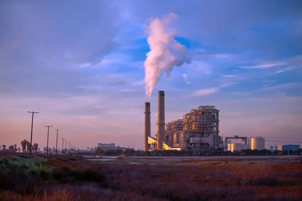 Natural gas power plant with two tall smokestacks against blue and purple sunset sky